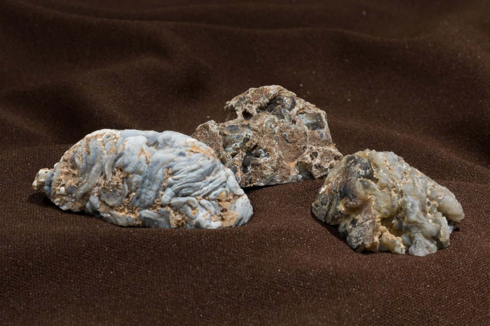 The blue and brown exterior of 3 small geodes that look like 3 small rocks.