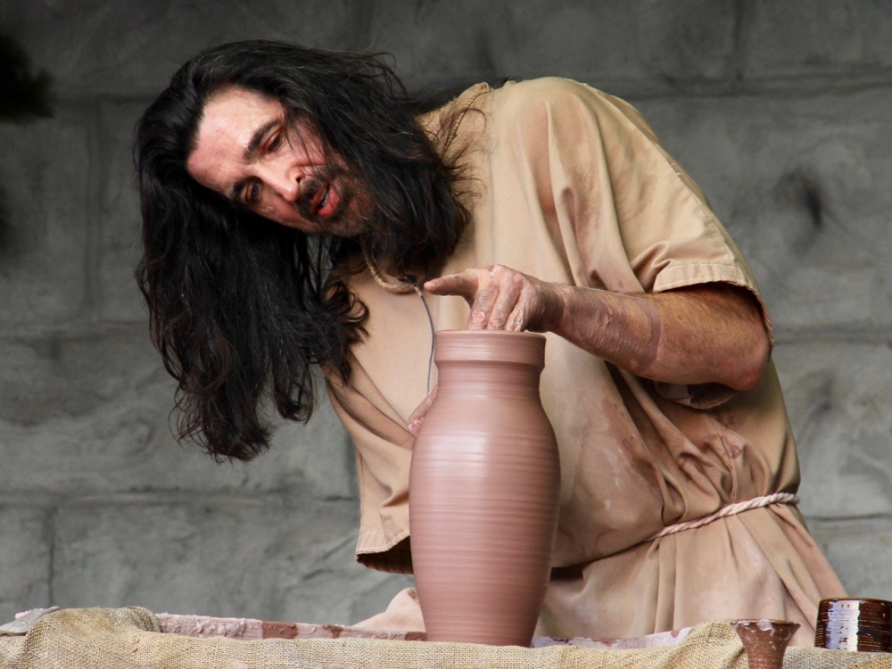 A potter putting the finishing touches on top of a tall vase on potter's wheel.