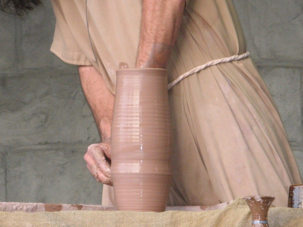 A potter with arm inside a tall vase he is making on the potter's wheel.