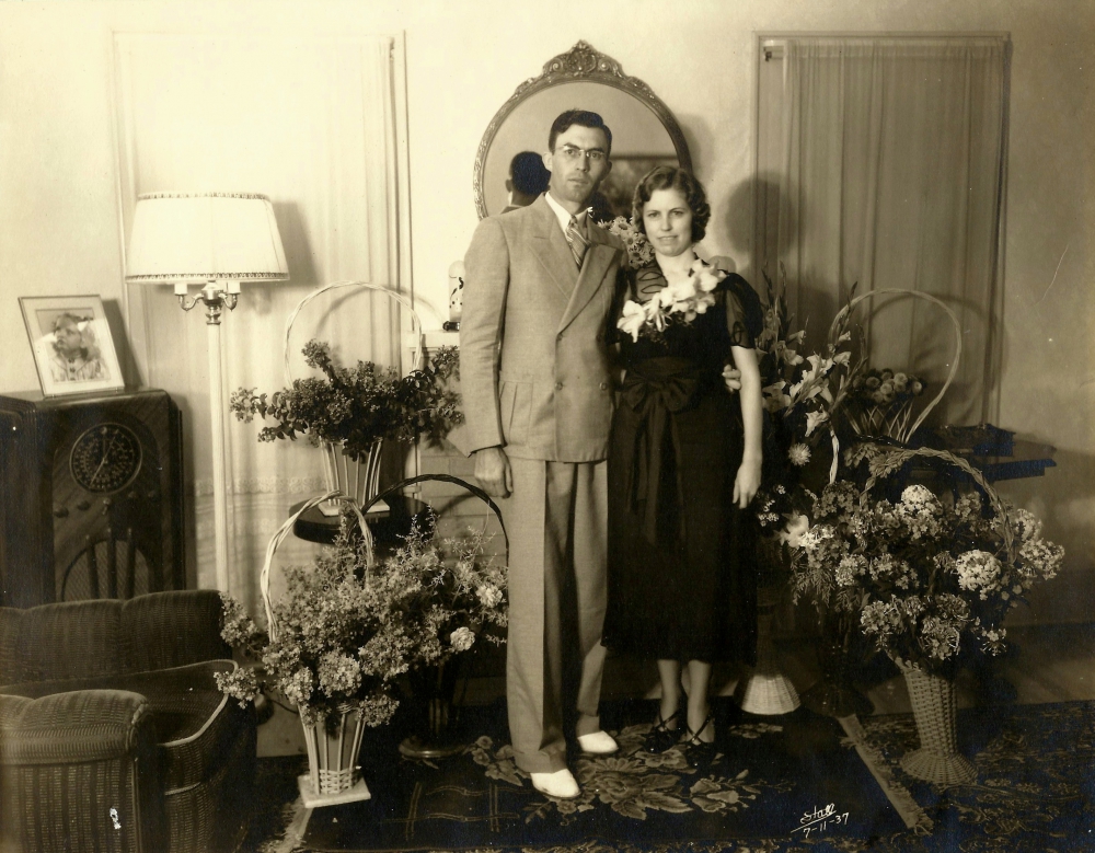 Young couple facing camera who just married in a 1930s era home surrounded by flowers.