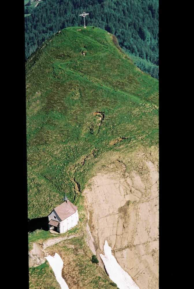 Small neo-Gothic chapel, Klimsenkapelle, on summit of Klimsenhorn with a large cross on the mountain peak above chapel.