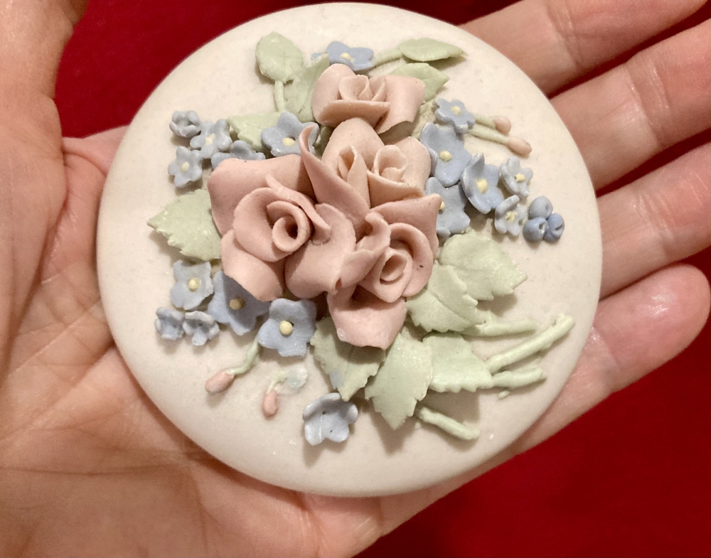 Small ornate ceramic lid covered with pink roses, blue flowers and green leaves.