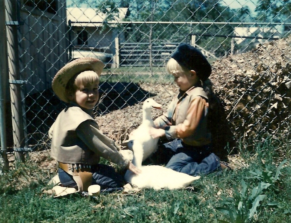 Two young boys playing with their ducks outside. One wearing cowboy hat and the other has on a Daniel Boon hat.