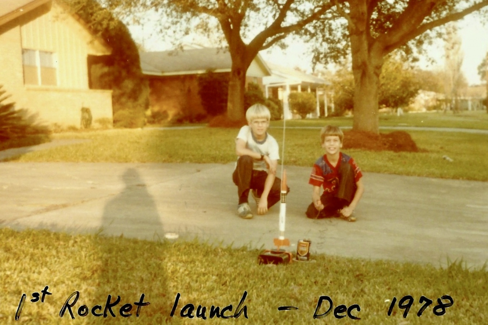 Two young boys getting ready to launch their small rocket on the driveway in front of their home.