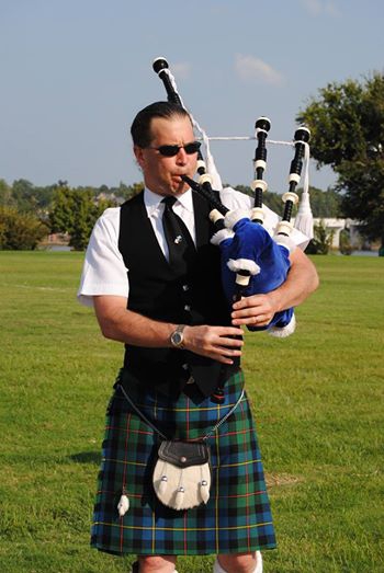 Charles Kester playing his bagpipe on a sunny day outside at a funeral.