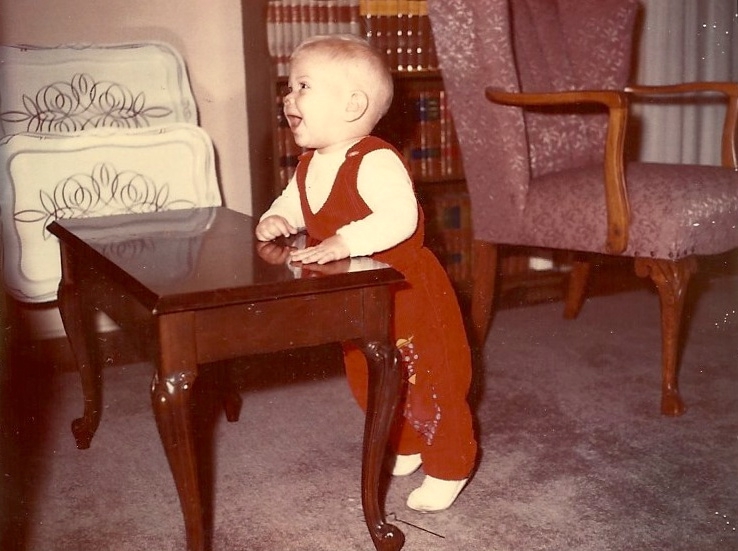 An 11-month old boy happily singing as he stands by the piano bench.