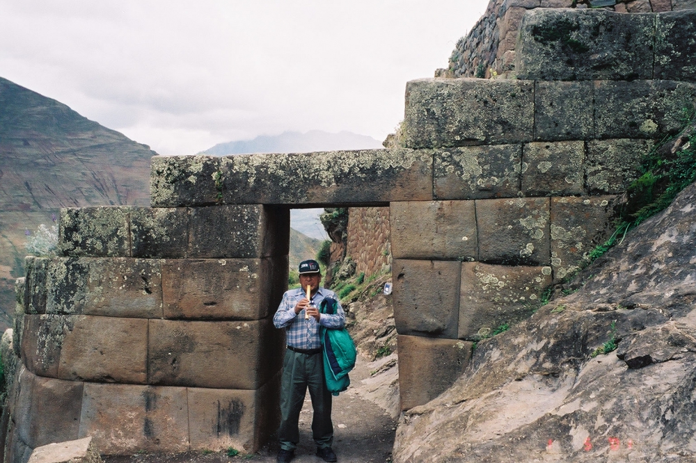 A man is standing in the doorway of an Inca Ruin and playing one of the flutes of the Incas.