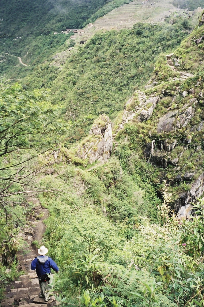 Monty Kester can be seen hiking on a long winding mountain path from Huayna Picchu toward Machu Picchu in the distance.