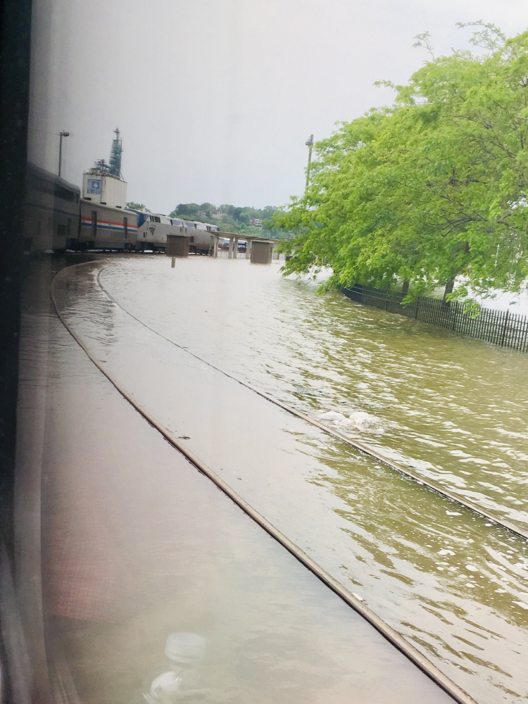 View from train window showing train track and train arching in curve just barely above the water of the flood.