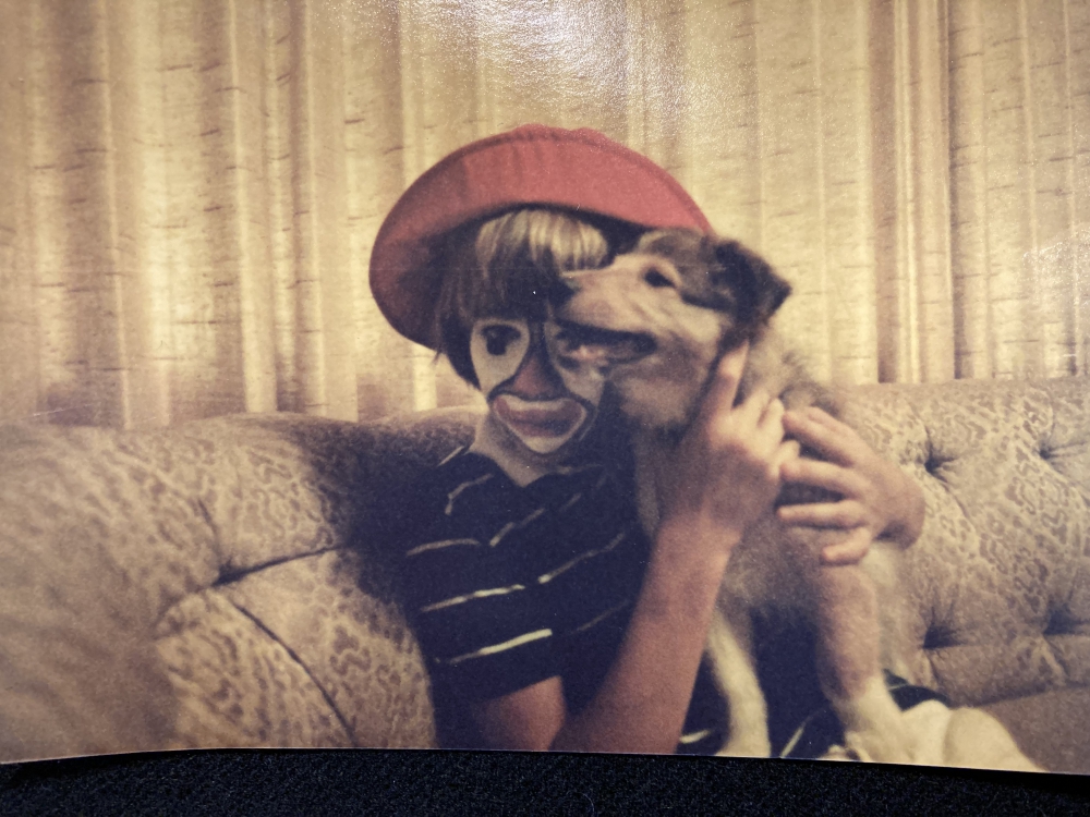 A young teenage boy in clown-face holding his tan colored Sheltie dog.