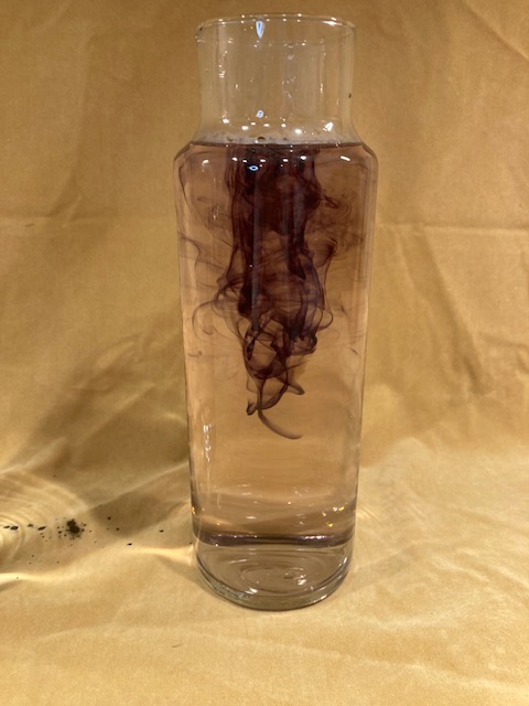 Several drops of black ink swirling around in a tall glass column of water.