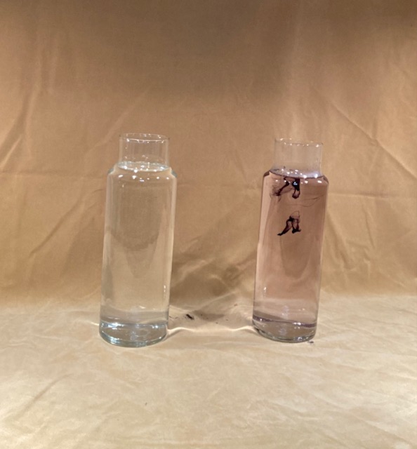 Two glass columns of water, the left one pure and the right one has drops of ink showing in it.