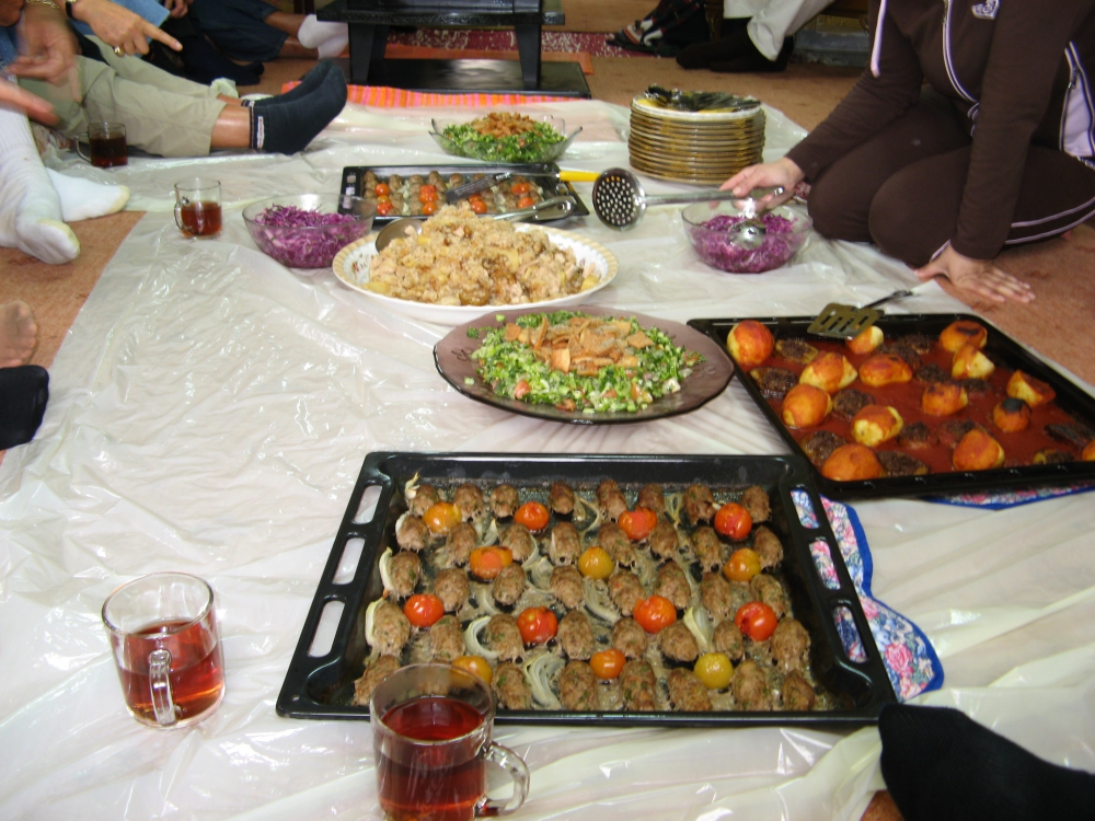 Shows feet of people gathered around platters of Israeli food on the floor.