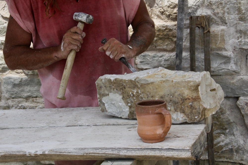 Shows the hands of a stone cutter as he chisels on a stone to shape it.