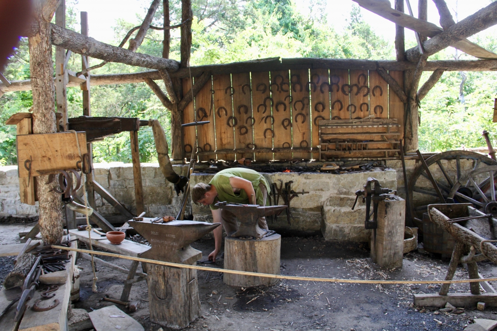 Open air blacksmith shop showing forge and anvil plus some of work done.