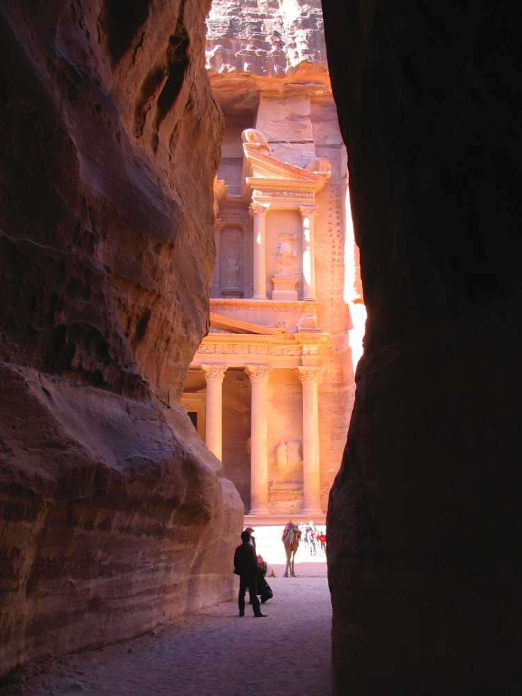 Looking at a sliver of Petra's Treasury building glowing in the sunlight from the darkness of passageway, the Siq.