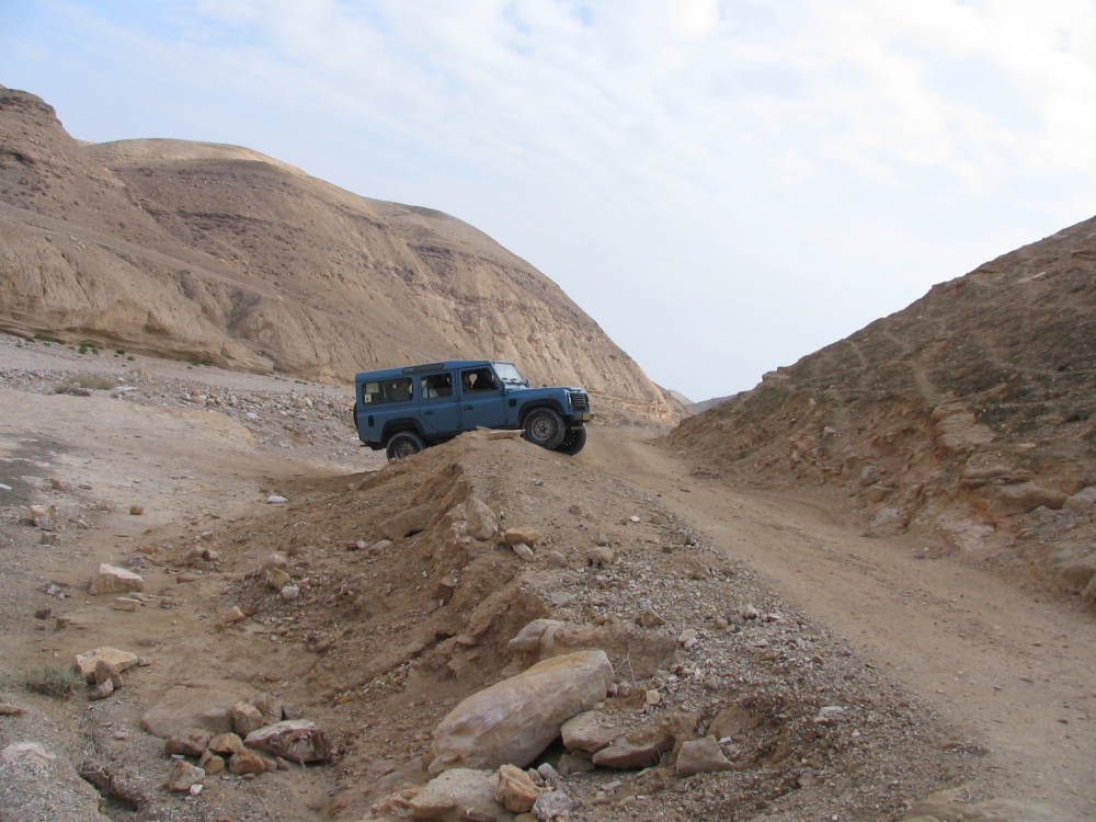 A Jeep struggling up a steep rise as it exits a dry riverbed in the Judean Desert.