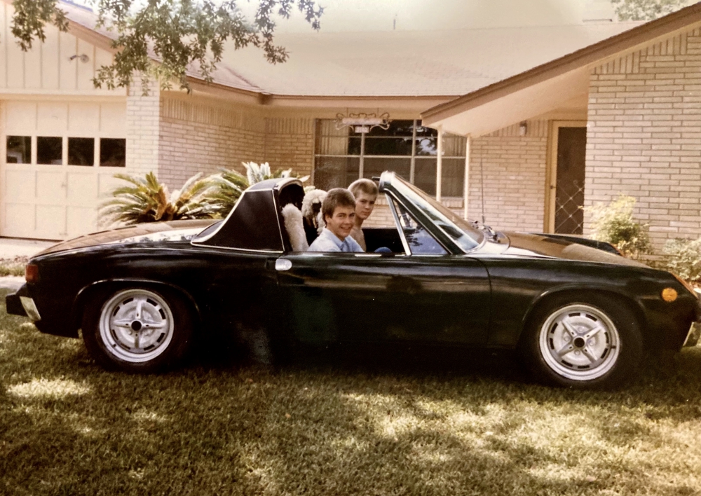 Two boys in green Porsche 914 in front of a house.