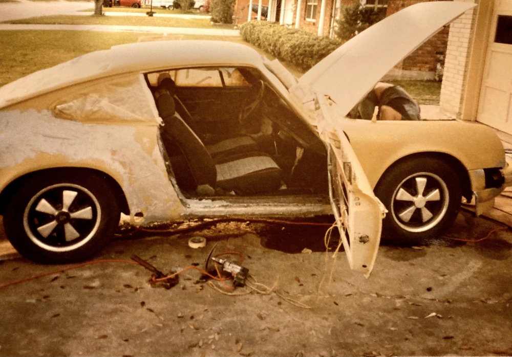 Porsche 911 with evidence of Bondo filler in front of house as teen works on it.