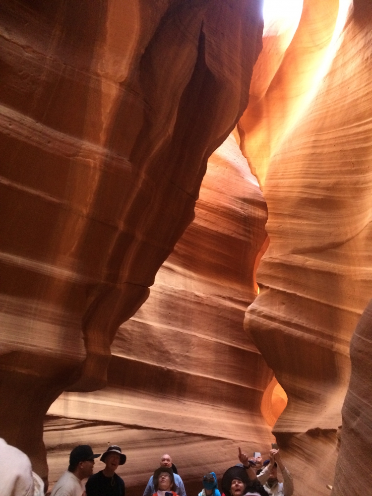 People dwarfed by water shaped and colorful sandstone above them in Upper Antelope Slot Canyon.