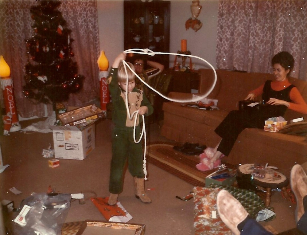 picture of young boy in cowboy outfit trying to rope something in the living room.