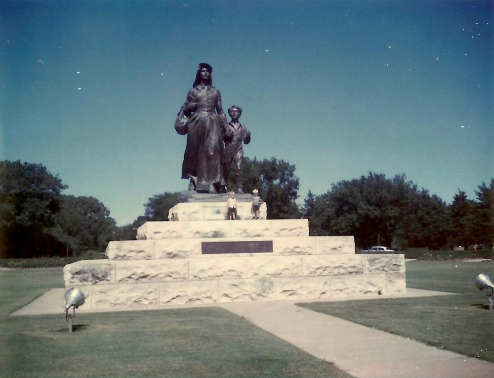 Two small boys standing on the base with the large Pioneer Woman statue towering above them.