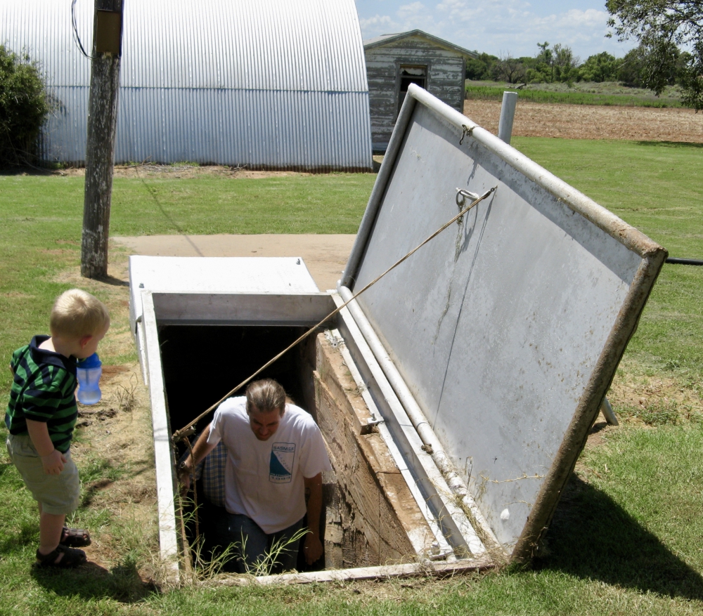 On a farm in Texas, a man, Charles Kester, is seen coming up the steps of an open underground storm shelter with a young boy standing at the top and watching him.